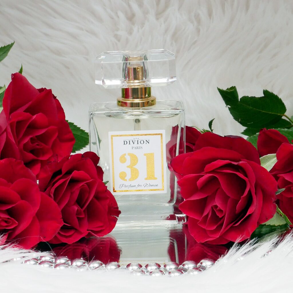 Lane perfumy Divion 31 – kompozycja na lustrze z różami Lane perfumy Divion 31 stojące na lustrze w otoczeniu czerwonych róż.