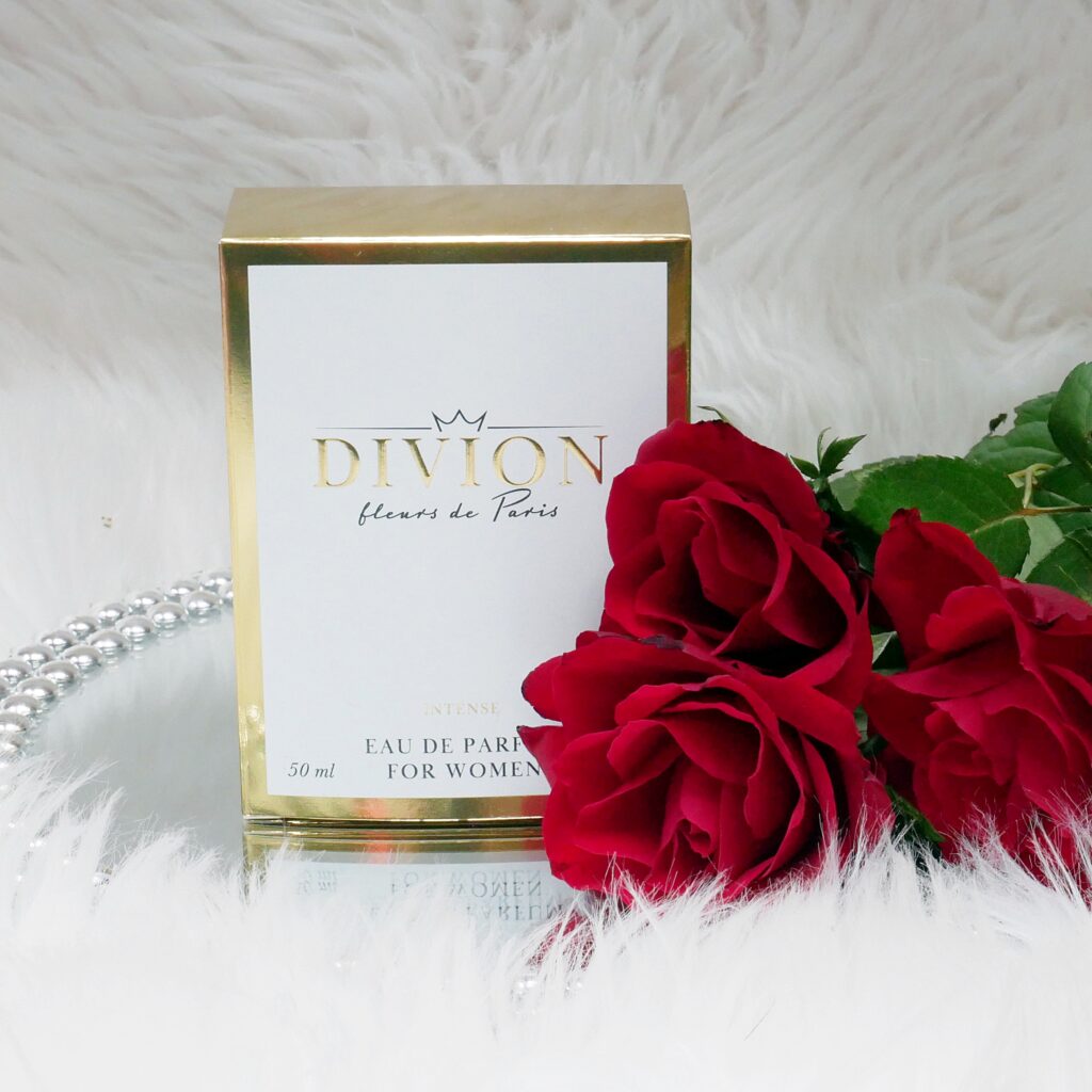 Opakowanie lanych perfum Divion Intense Fleurs de Paris Eleganckie biało-złote pudełko lanych perfum Divion Intense Fleurs de Paris w otoczeniu róż.