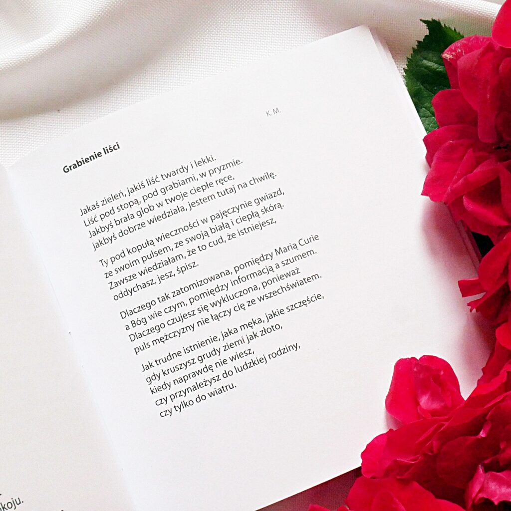 Wiersz „Grabienie liści” – Elżbieta Juszczak „Pasterze dolin” Otwarty tomik poezji na stronie z wierszem „Grabienie liści” w kompozycji z czerwonymi różami.