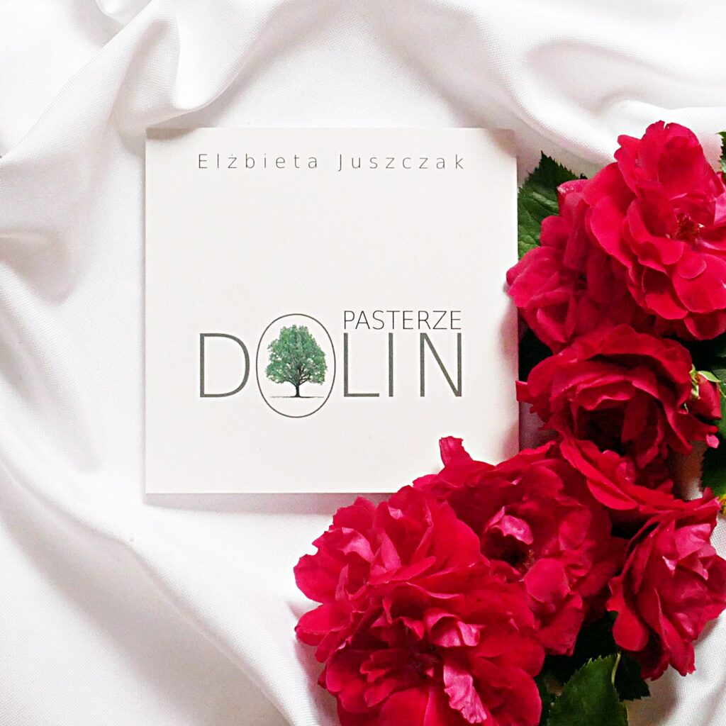 Elżbieta Juszczak „Pasterze dolin” - recenzja tomiku poezji Okładka tomiku poezji „Pasterze dolin” autorstwa Elżbiety Juszczak leżąca na białym materiale w otoczeniu czerwonych róż.