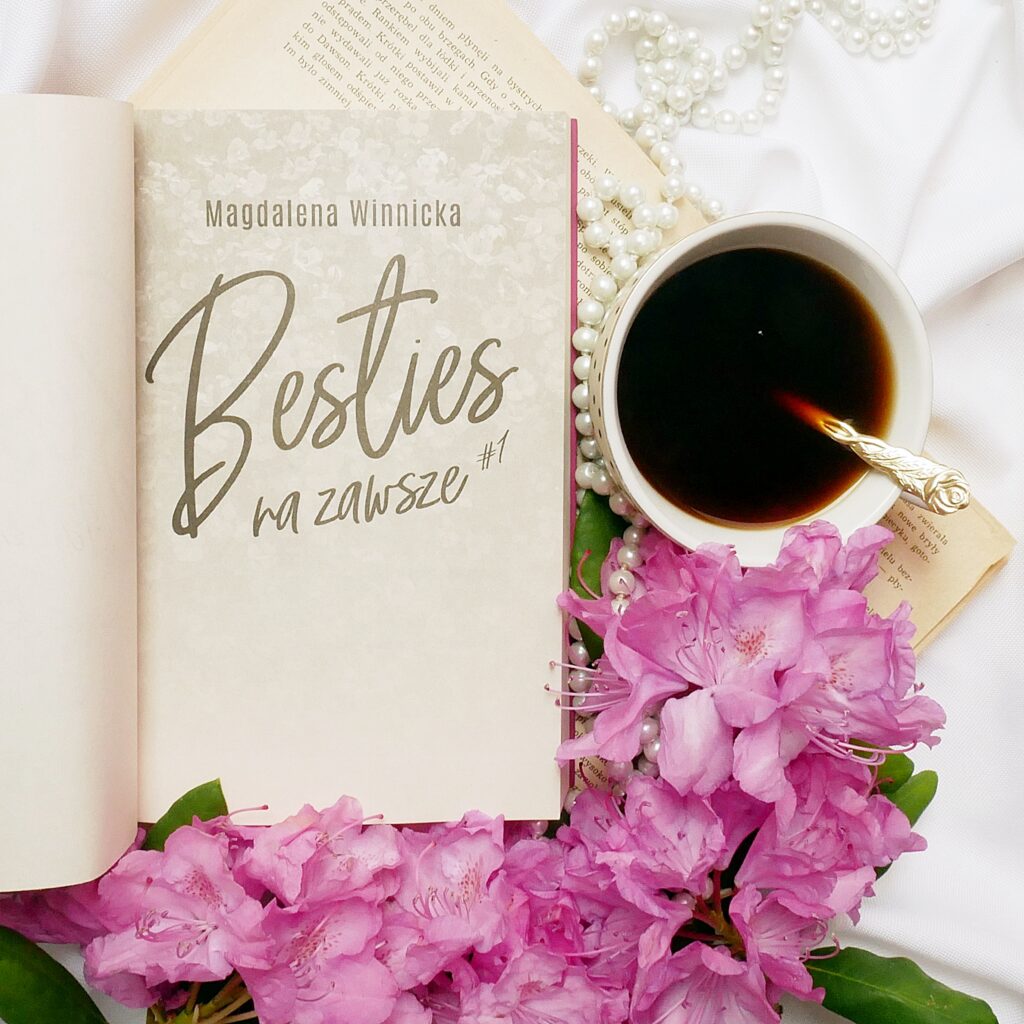 Strona tytułowa książkiMagdalena Winnicka „Besties na zawsze” w otoczeniu różwych kwiatów, pereł oraz filiżanki kawy na białym tle.