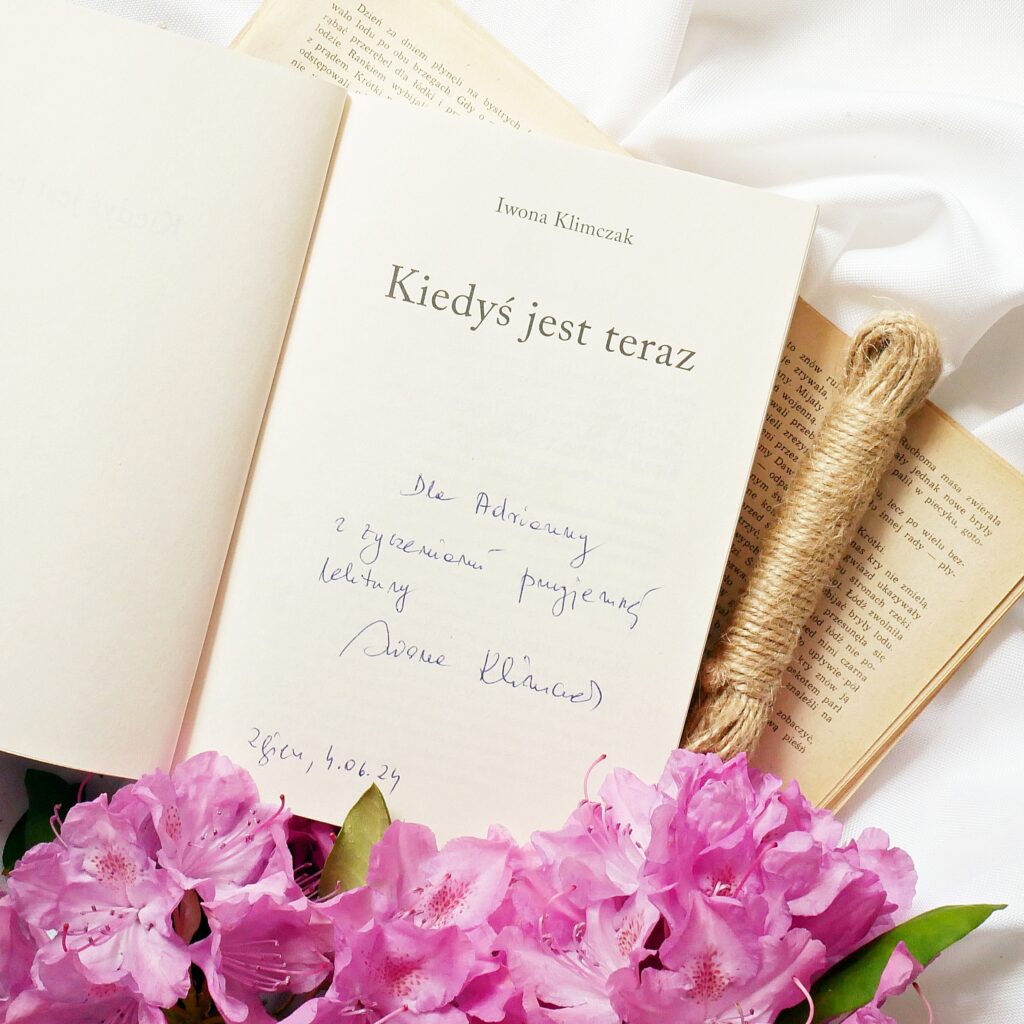 Strona tytułowa książki „Kiedyś jest teraz” autorstwa Iwony Klimczak Strona tytułowa książki „Kiedyś jest teraz” autorstwa Iwony Klimczak z dedykacją. Obok leży sznurek i kwiaty rododendrona