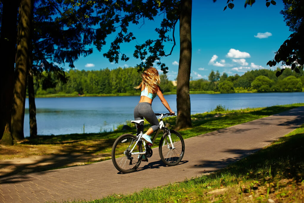 Kobieta na rowerze nad jeziorem, symbolizująca regenerację i aktywny wypoczynek, które są kluczowe dla zachowania work-life balance.