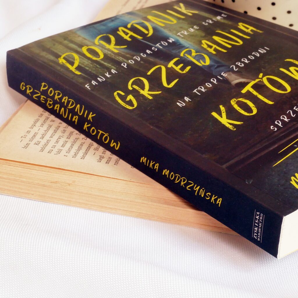 Grzbiet i okładka książki „Poradnik grzebania kotów” Miki Modrzyńskiej Grzbiet i okładka książki „Poradnik grzebania kotów” Miki Modrzyńskiej.  Stara książka i filiżanka z kawą w tle