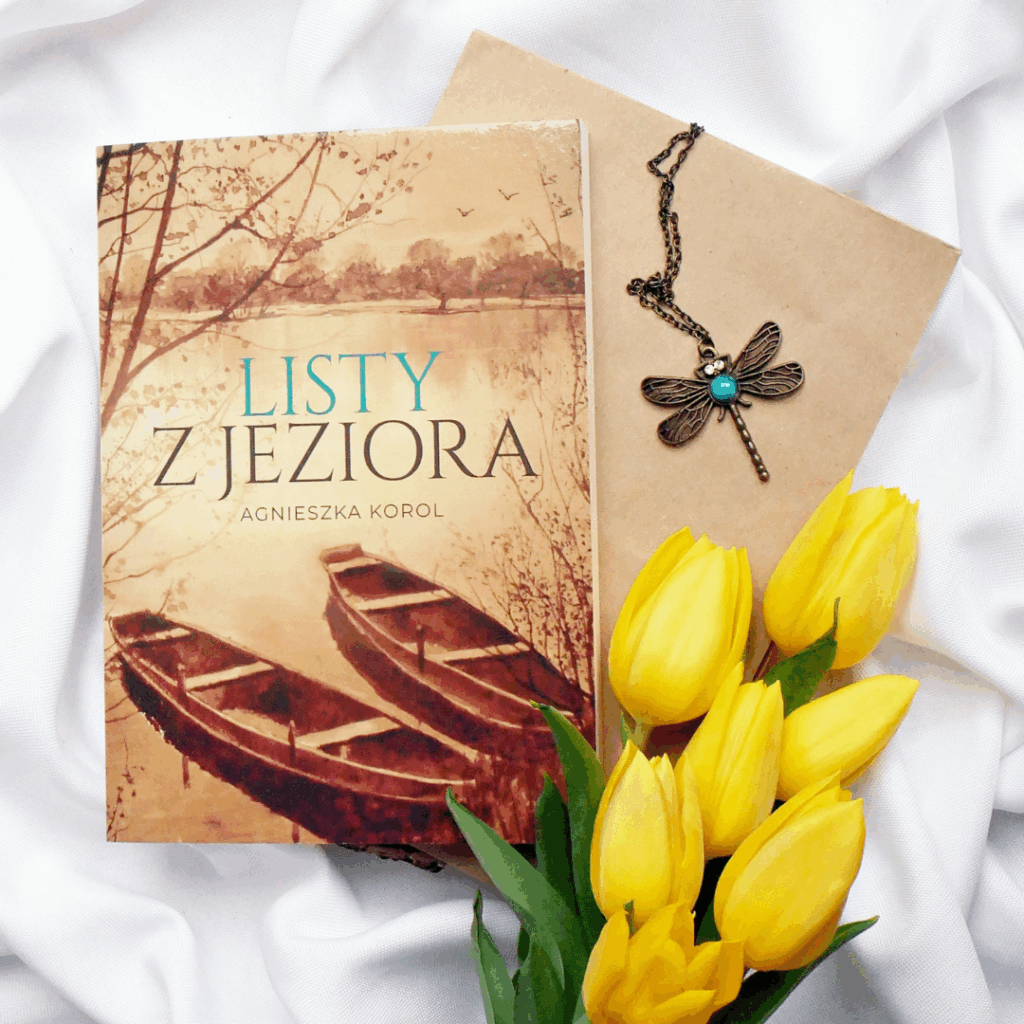 Okładka książki „Listy z jeziora” Agnieszki Korol. Leży na plastrze drewna, obok niej koperta, naszyjnik z ważką i żółte tulipany