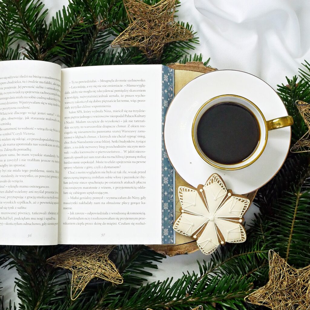 Wnętrze książki „Świąteczna zamiana” – fragment tekstu. Rozłożona książka prezentująca treść rozdziału, ułożona na drewnianym krążku w otoczeniu świątecznych dekoracji, złotych gwiazdek i gałązek choinki.