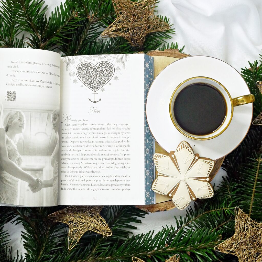 Rozdział poświęcony bohaterce o imieniu Nina Otwarta książka na stronie rozpoczynającej rozdział „Nina” z ozdobną grafiką serca i kotwicy. Obok filiżanka kawy i lukrowany pierniczek.