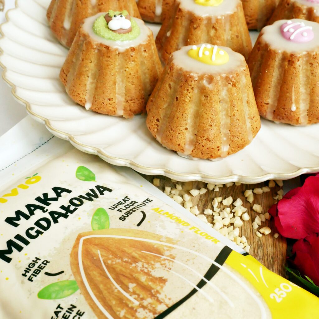 Bezglutenowa mąka migdałowa Fivio obok gotowych babeczek i posiekanych orzechów na drewnianej desce.
