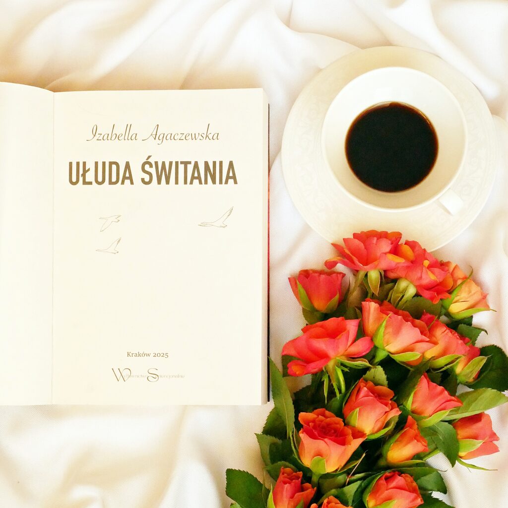 Strona tytułowa książki „Ułuda świtania” autorstwa Izabelli Agaczewskiej. Obok stoi filiżanka z kawą oraz pomarańczowe róże.