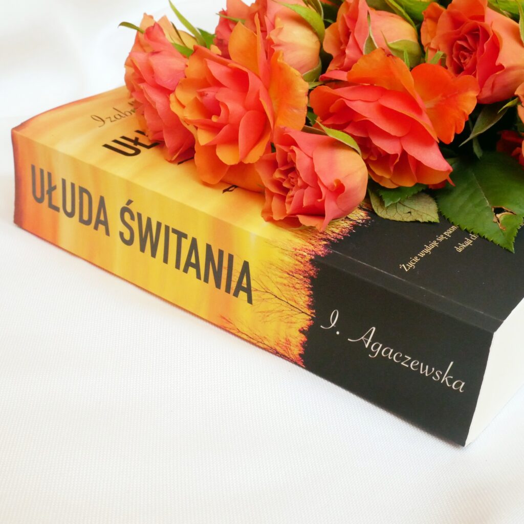 Grzbiet i okładka książki „Ułuda świtania” Izabelli Agaczewskiej. W tle pomarańczowe róże.