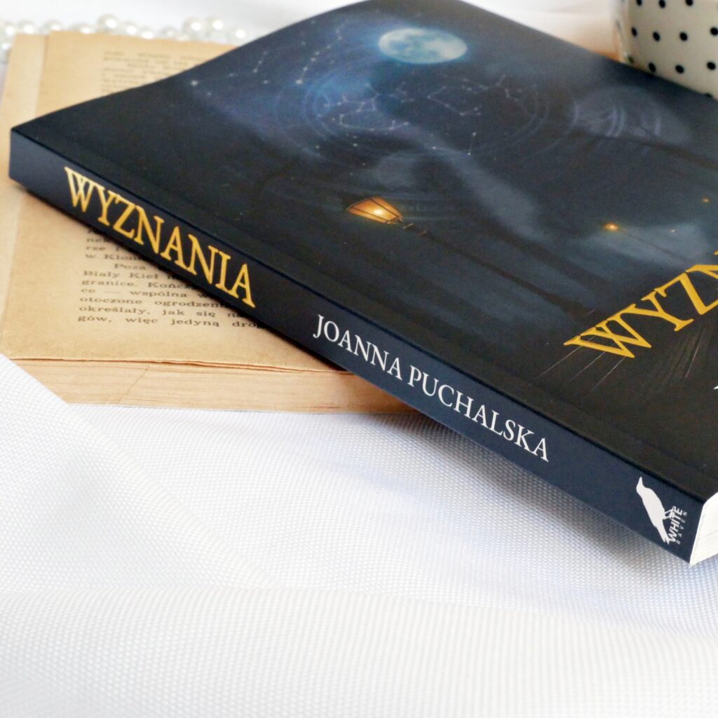 Grzbiet i okładka książki „Wyznania” Joanny Puchalskiej Grzbiet i okładka książki „Wyznania” Joanny Puchalskiej z perłami i filiżanką kawy w tle.