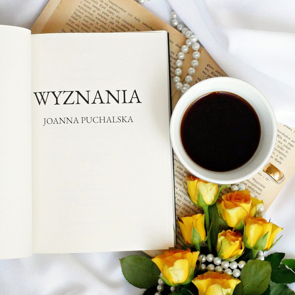 Strona tytułowa książki „Wyznania” autorstwa Joanny Puchalskiej Strona tytułowa książki Joanna Puchalska „Wyznania” z motywem nocnego nieba, gwiazdozbiorów i latarni. Obok leży filiżanka kawy i żółte róże.