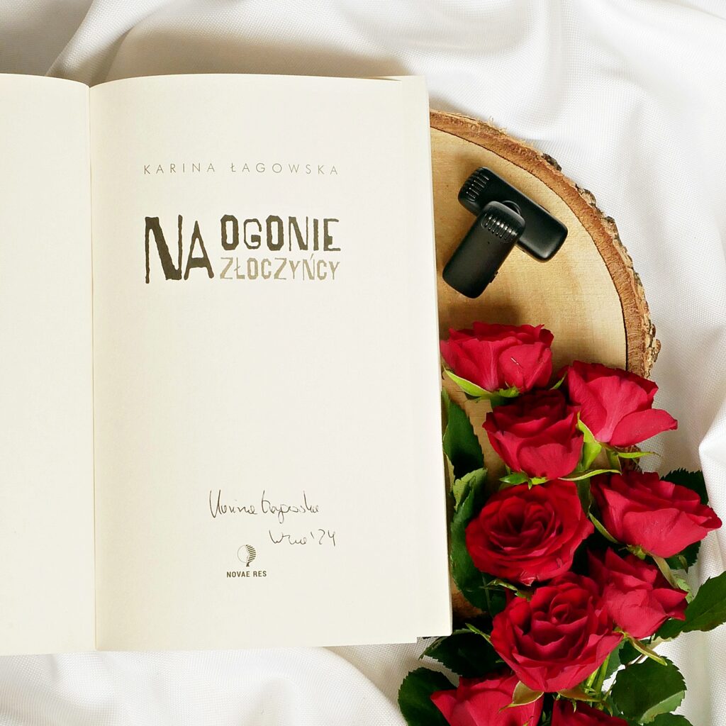 Strona tytułowa książki „Na ogonie złoczyńcy” autorstwa Kariny Łagowskiej. Obok leżą dwa mikrofony i czerwone róże.