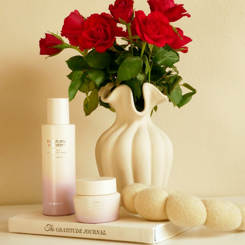 Esencja z probiotykiem i krem z ceramidami Haruharu Wonder Black Rice obok wazonu z czerwonymi różami.