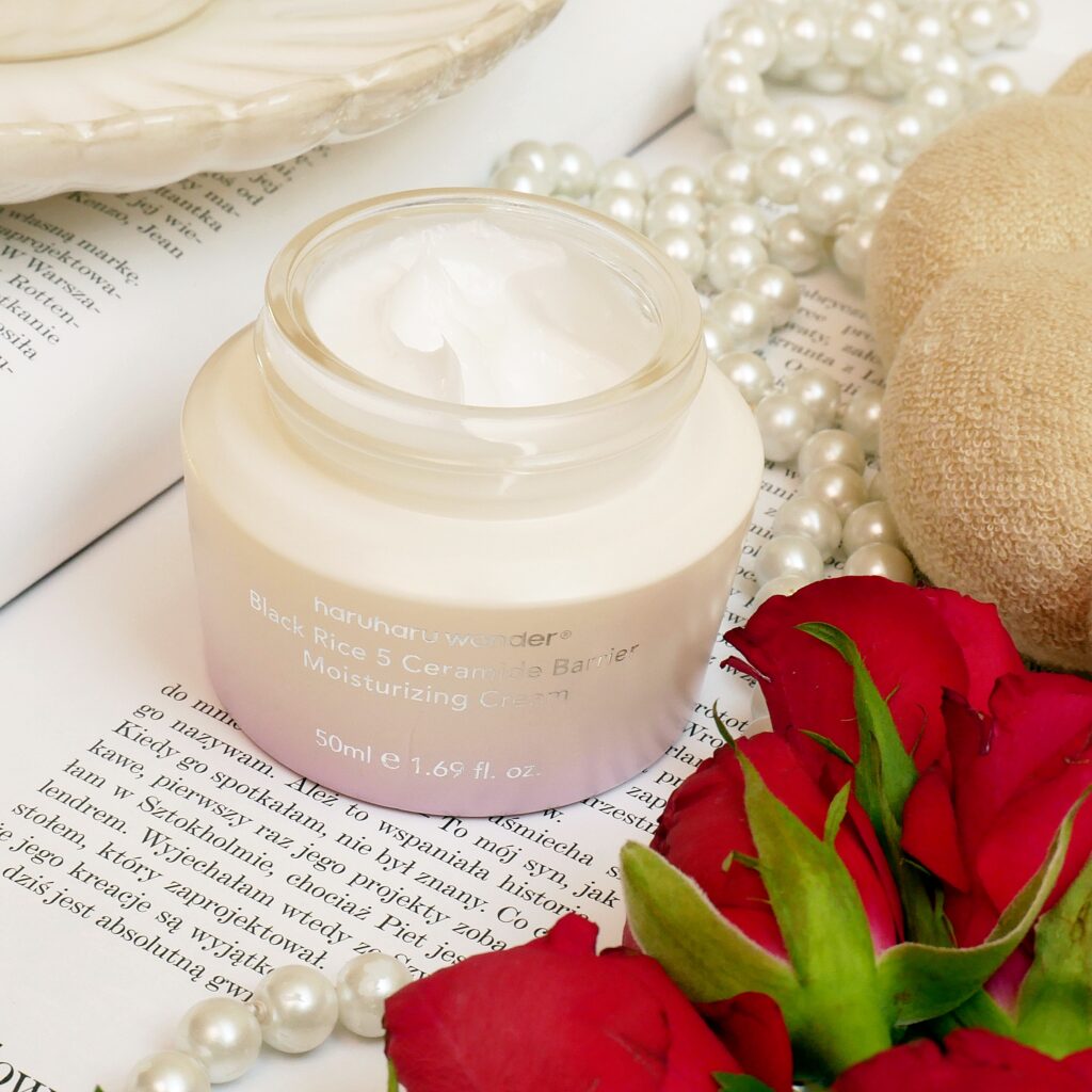 Otwarty słoiczek kremu nawilżającego z ceramidami Haruharu Wonder Black Rice w otoczeniu pereł i czerwonych róż.