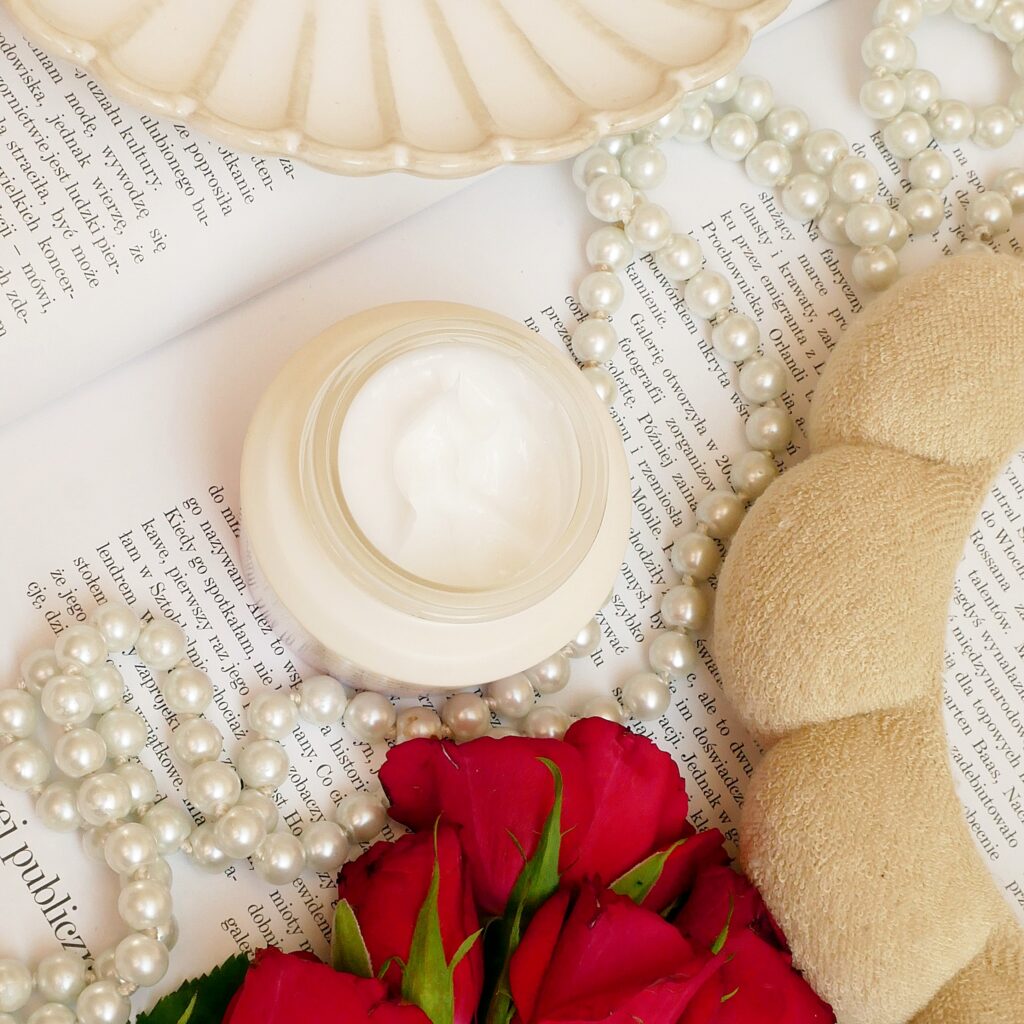 Widok z góry na otwarty krem z czarnym ryżem i ceramidami  na tle magazynu, czerwonych róż i i pereł.