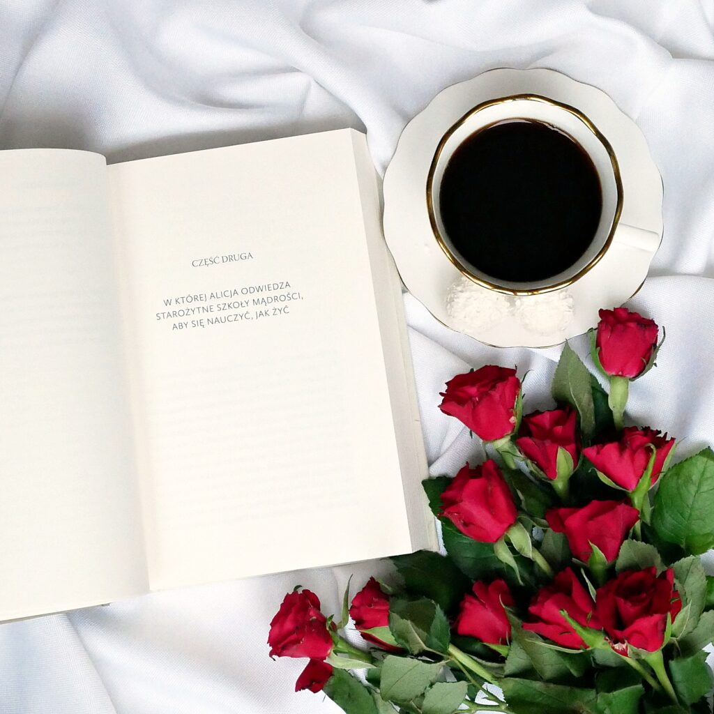 Strona z napisem: „Część druga, w której Alicja odwiedza starożytne szkoły mądrości”, widoczna kawa i róże.