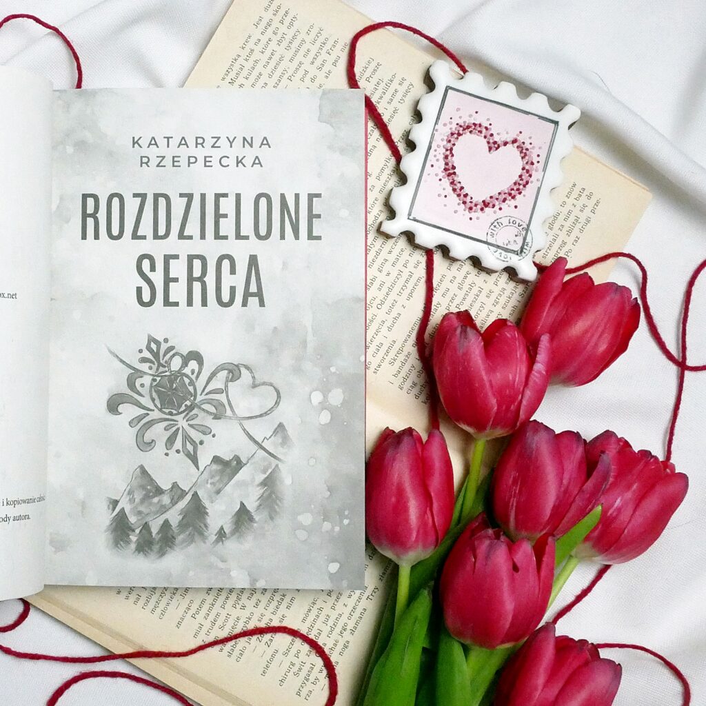 Strona tytułowa książki „Rozdzielone serca” autorstwa Katarzyny Rzepeckiej Strona tytułowa książki „Rozdzielone serca” Katarzyny Rzepeckiej w otoczeniu czerwonych tulipanów i piernika w kształcie znaczka pocztowego z sercem