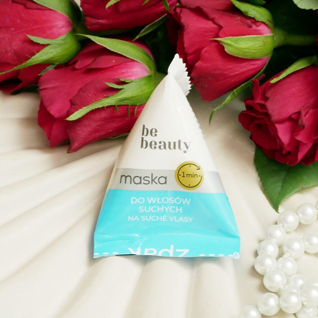 Intensywnie nawilżająca niebieska maska Be Beauty do włosów suchych Niebieska saszetka maski do włosów suchych Be Beauty na beżowej tacy w otoczeniu pereł i czerwonych róż.