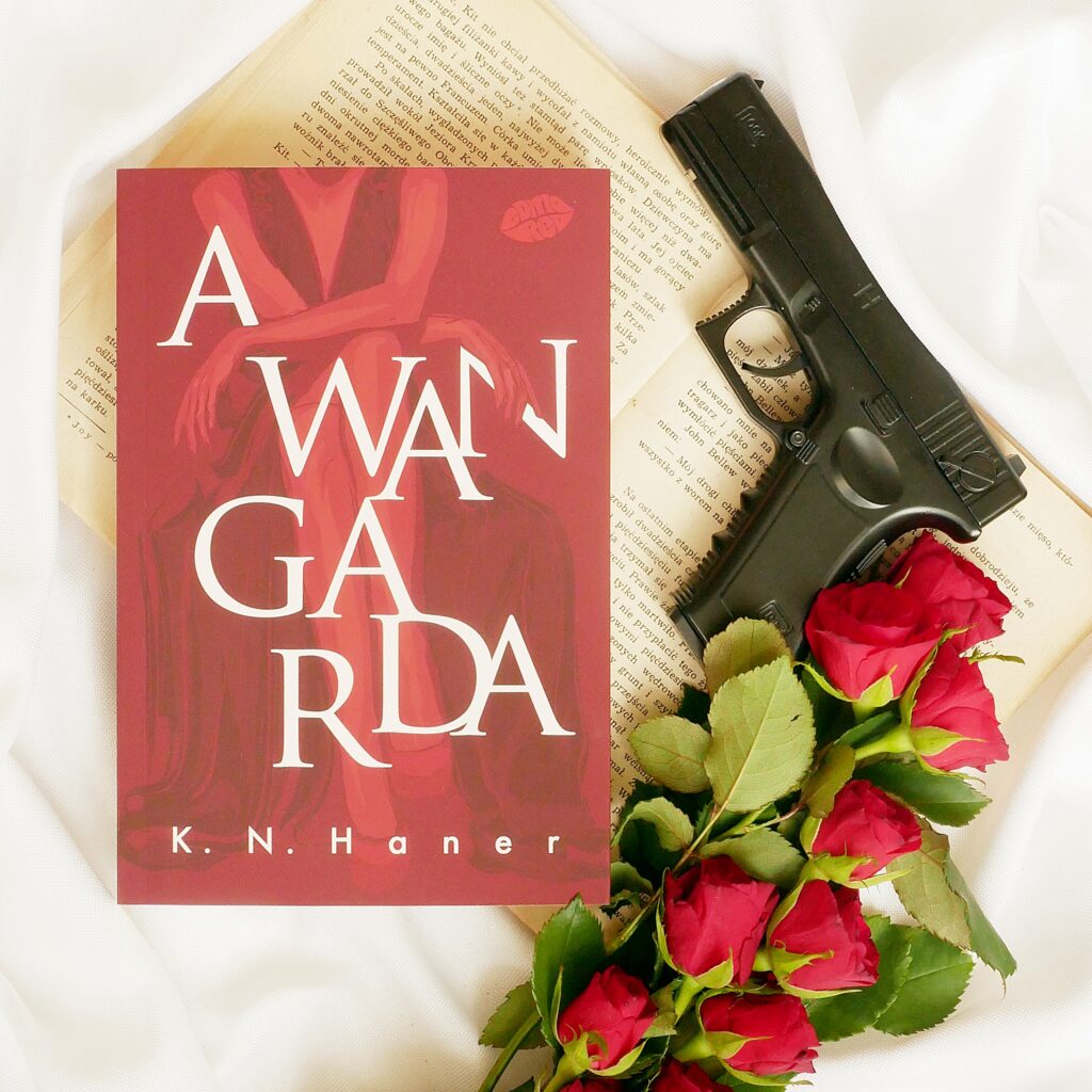 Recenzja książki „Awangarda” K.N. Haner Okładka książki „Awangarda” K.N. Haner. Obok leży pistolet, perły i czerwone róże.