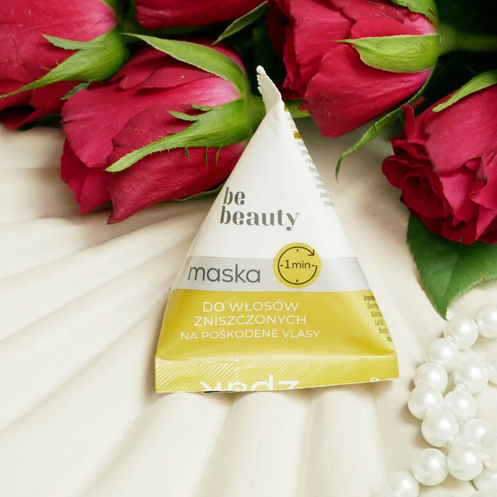 Żółta maska Be Beauty do włosów zniszczonych Żółta maska do włosów zniszczonych Be Beauty w kształcie piramidki leżąca na ozdobnej, falowanej tacy z perłami i czerwonymi różami.