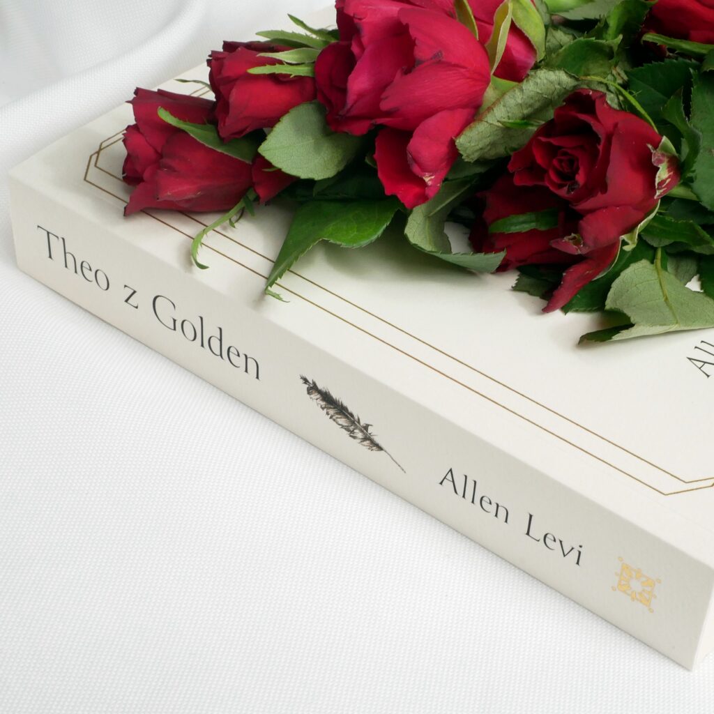 Grzbiet i okładka książki „Theo z Golden” Allena Leviego od Wydawnictwa Media Rodzina. Książka leży na białym materiale, a na niej bukiet czerwonych róż.