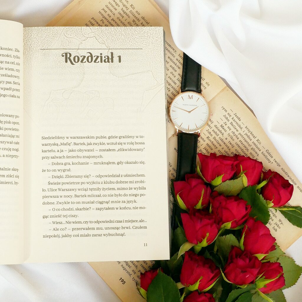 Otwarta książka na stronie z pierwszym rozdziałem, kompozycja z eleganckim zegarkiem i czerwonymi różami.