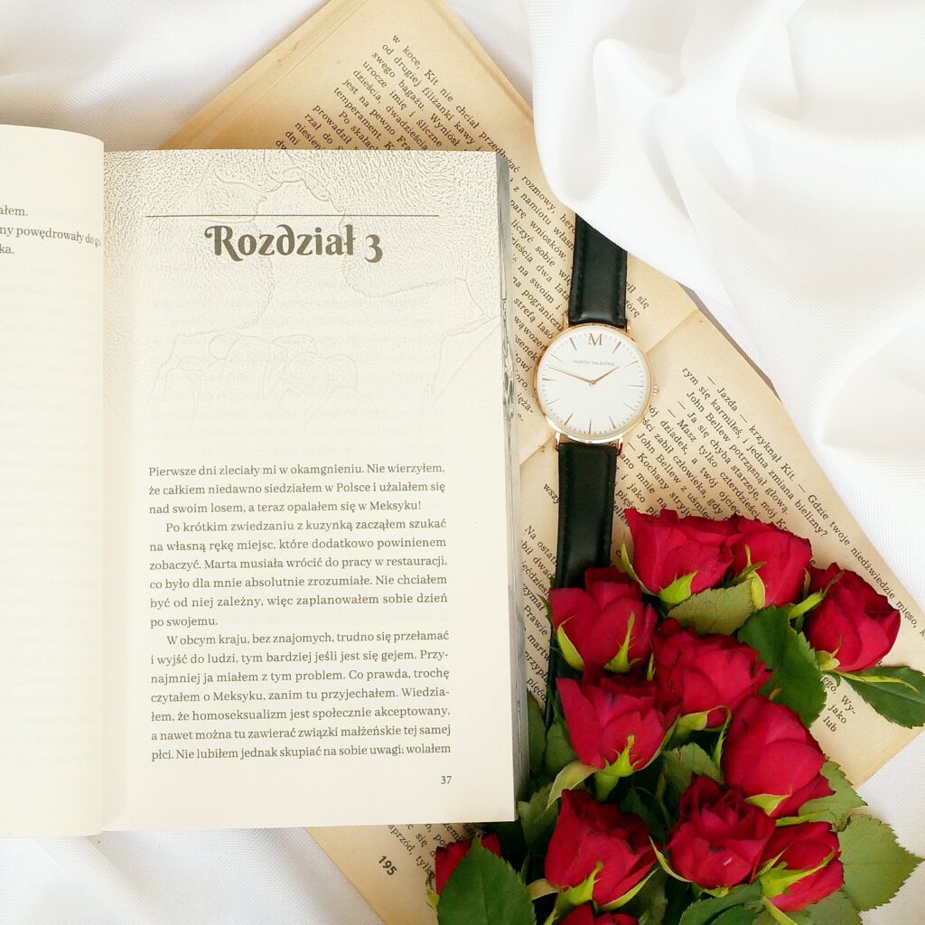 Otwarta książka na stronie z trzecim rozdziałem, kompozycja z eleganckim zegarkiem i czerwonymi różami.