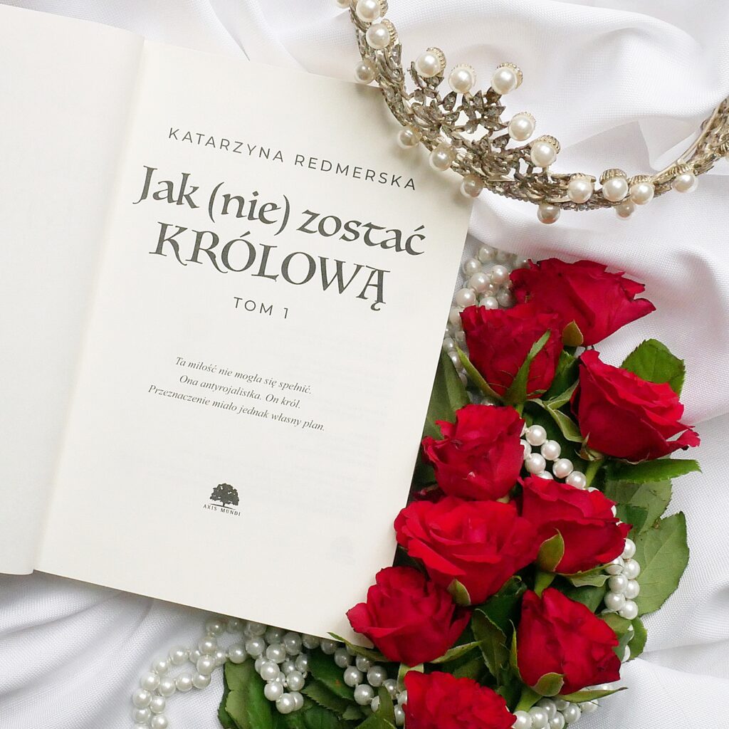Katarzyna Redmerska „Jak (nie) zostać królową”. Strona tytułowa książki w romantycznej kompozycji flat lay z czerwonymi różami, perłami i koroną.