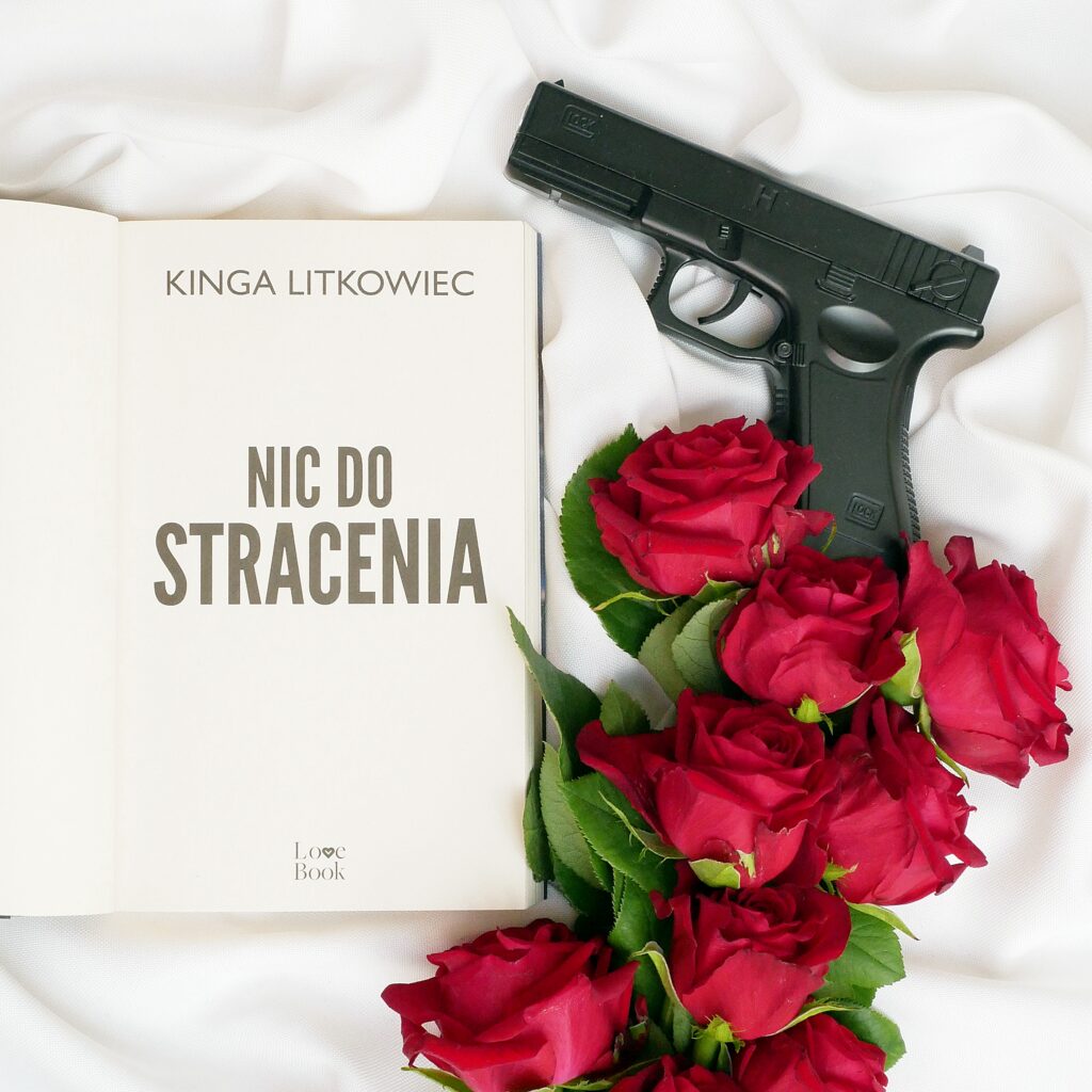 Strona tytułowa książki Kingi Litkowiec „Nic do stracenia” Strona tytułowa książki z napisem Kinga Litkowiec „Nic do stracenia”, w aranżacji z repliką pistoletu i czerwonymi różami.