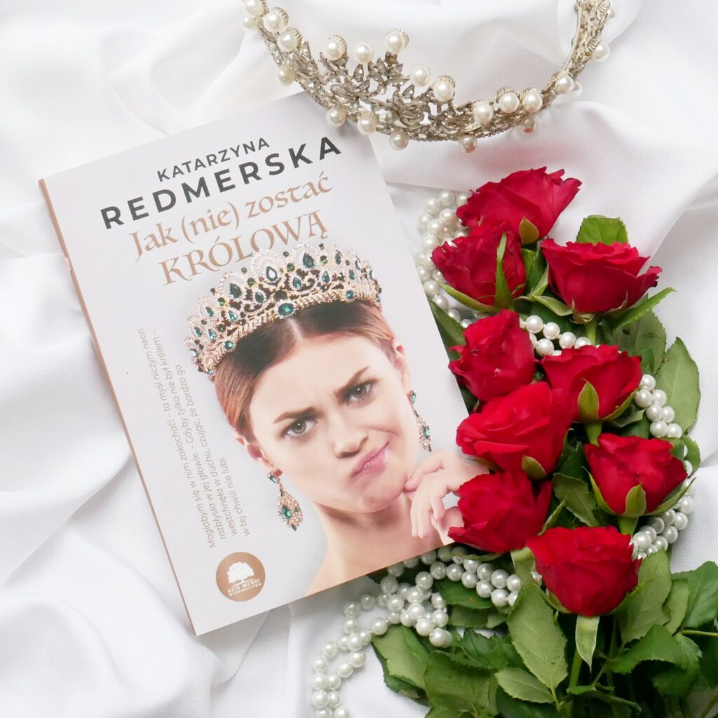 Katarzyna Redmerska „Jak (nie) zostać królową”. Okładka książki w kompozycji z czerwonymi różami, perłami i koroną.