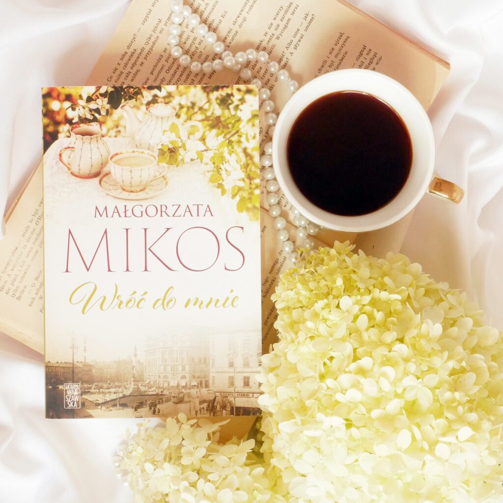 Małgorzata Mikoś „Wróć do mnie” - recenzja Okładka książki Małgorzaty Mikoś „Wróć do mnie” w romantycznej aranżacji z filiżanką kawy, perłami i białymi kwiatami.