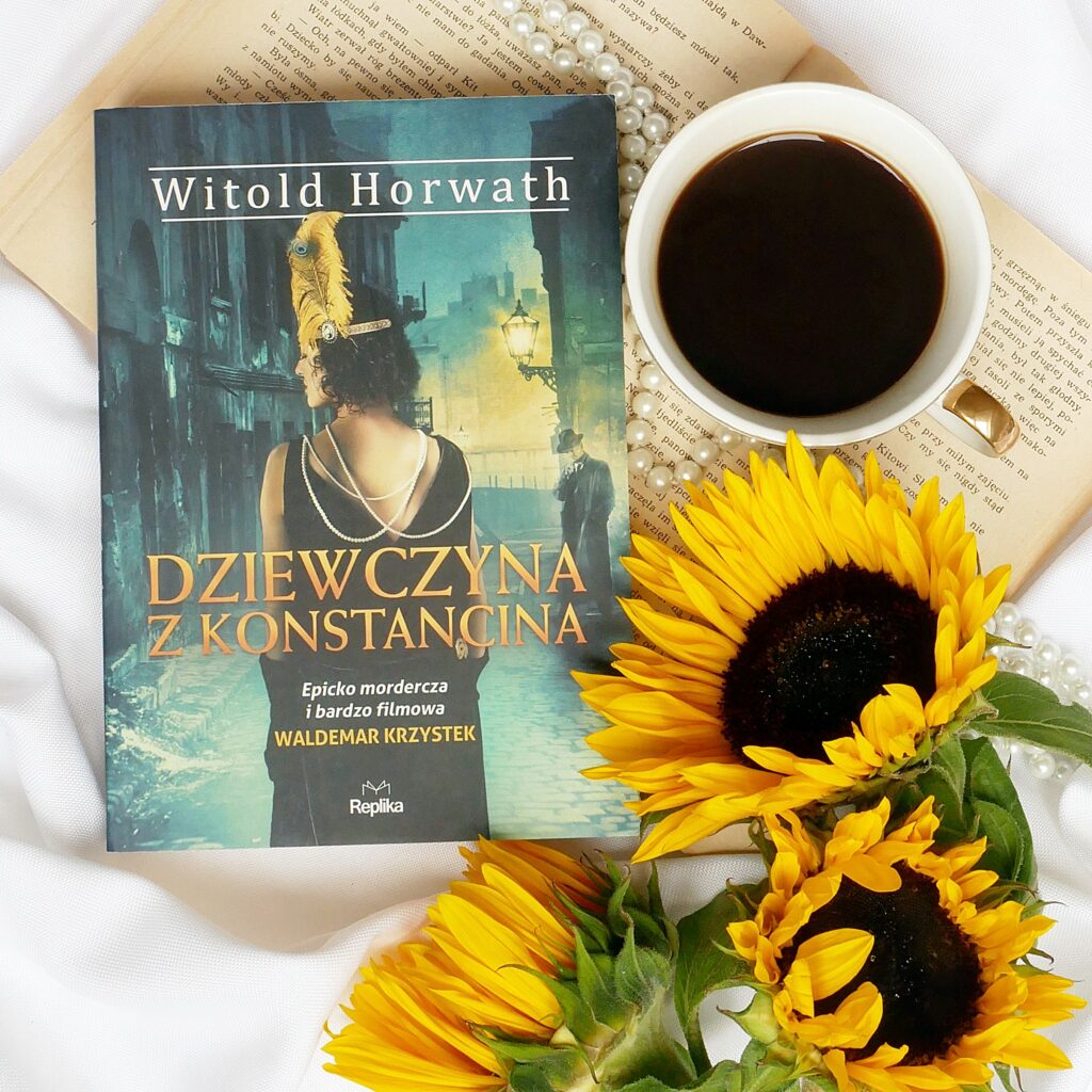 Okładka książki Witolda Horwatha „Dziewczyna z Konstancina”. Leży na białym materiale w otoczeniu pereł, filiżanki czarnej kawy i trzech słoneczników.
