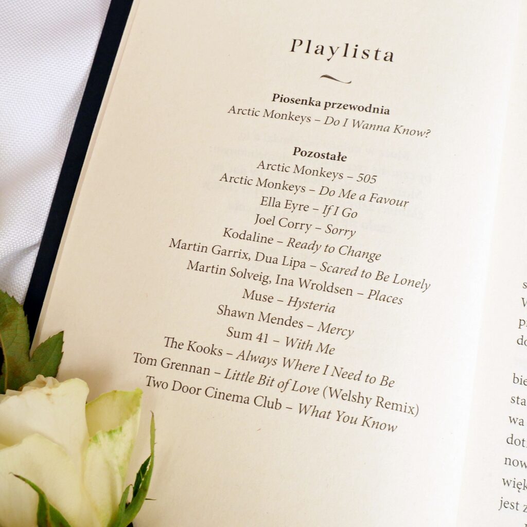 Strona z oficjalną playlistą z książki „Niepokorny driver” Weroniki Jaczewskiej, obok której leżą białe róże.